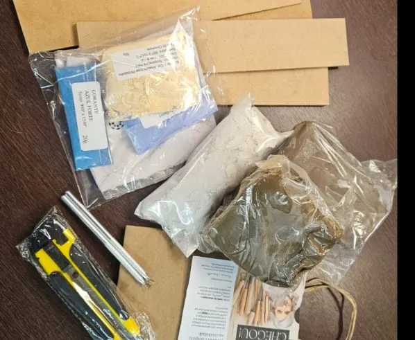 Kit de materiais aberto: argila, porcelana, vidrados, corante, estilete, réguas, estecas e bases de brinco sobre a mesa